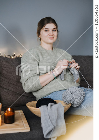 Person knitting on a cozy couch with candles, representing the slow living trend, mindfulness, and creative self-care practices. 120654253