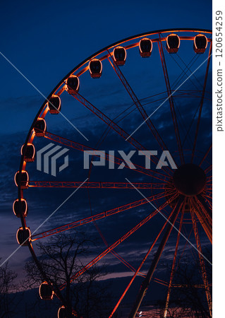 Ferris wheel with glowing red cabins against a deep blue night sky. Highlights urban nightscapes, amusement rides, and atmospheric lighting. Ferris wheel with glowing red cabins against a deep blue night sky. Highlights urban nightscapes, amusement rides, and atmospheric lighting. 120654259
