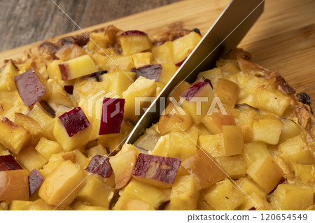 Cutting freshly baked sweet potato and apple quiche with a knife 120654549