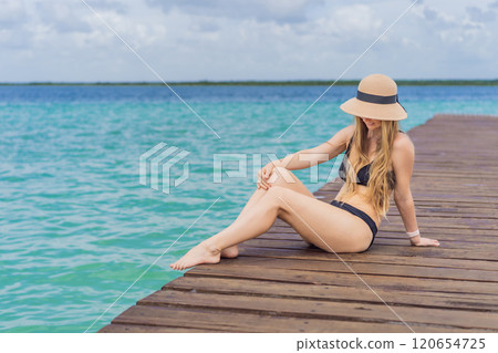 Woman in swimsuit sitting on a pier at Lake Bacalar. Quintana Roo, Mexico travel, summer relaxation, and waterfront serenity concept 120654725