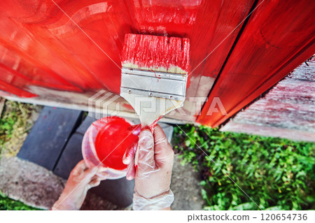 100 mm wide flat paintbrush in hand of house painter during process of painting front door of country house rich red colour. 100 mm wide flat paintbrush in hand of house painter during process of painting front door of country house rich red colour. 120654736