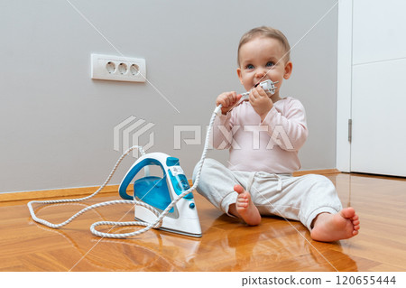 A baby exploring an iron cord while sitting on the floor near an electrical outlet, emphasizing the need for safety and caution. A baby exploring an iron cord while sitting on the floor near an electrical outlet, emphasizing the need for safety and caution. 120655444