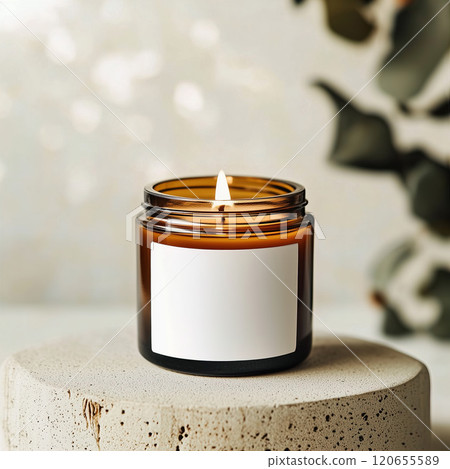 A candle that has a white label is currently sitting on a concrete block Amber glass jar candle white label mockup, boho style home interior. 120655589