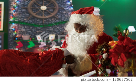 African american santa preparing his sack full of gifts in wrapping paper, delivering presents to wishful children around the world. Father Christmas decorating boxes with ribbons. Camera A. African american santa preparing his sack full of gifts in wrapping paper, delivering presents to wishful children around the world. Father Christmas decorating boxes with ribbons. Camera A. 120657562