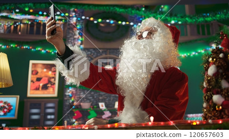 Aged Saint Nicholas taking pictures wearing the festive x mas suit, having fun with the winter holiday traditions. Santa takes selfies on his phone to spread the Christmas spirit. Camera B. Aged Saint Nicholas taking pictures wearing the festive x mas suit, having fun with the winter holiday traditions. Santa takes selfies on his phone to spread the Christmas spirit. Camera B. 120657603