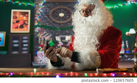 Saint Nick navigates web on his mobile phone checking lists and locations for delivery on world map. North Pole cabin with Christmas lights and magic, holiday preparations. Camera B. Saint Nick navigates web on his mobile phone checking lists and locations for delivery on world map. North Pole cabin with Christmas lights and magic, holiday preparations. Camera B. 120657605