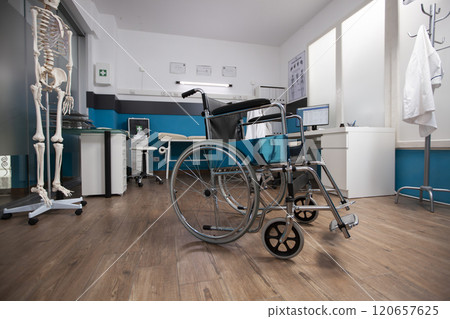 Medical wheelchair placed at center of empty doctors office with a desk and computer for medical consultation. Clinic room is filled with essential healthcare instruments and treatment aids. 120657625