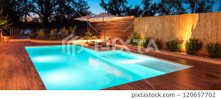 Luxurious poolside deck with night lighting and garden. Concept of evening leisure and tranquil outdoor retreat Luxurious poolside deck with night lighting and garden. Concept of evening leisure and tranquil outdoor retreat 120657702