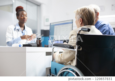Selective focus of elderly woman in wheelchair consulting with black doctor about post treatment care and health goals. African american female physician consulting with caucasian senior couple. 120657831