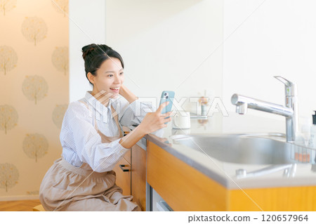 觀看一個智能手機的婦女在廚房裡 120657964