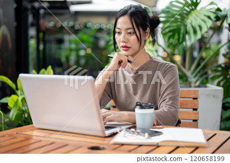 An attractive Asian woman sitting at an outdoor table of a cafe, working remotely. An attractive Asian woman sitting at an outdoor table of a cafe, working remotely. 120658199