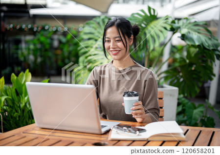A charming Asian woman working remotely from a serene green cafe, enjoying a coffee while working. A charming Asian woman working remotely from a serene green cafe, enjoying a coffee while working. 120658201