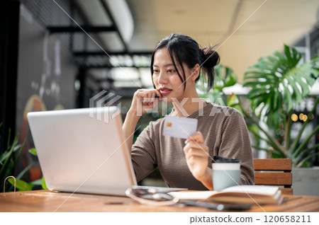 A charming, happy Asian woman is paying bills online or shopping online through her laptop. A charming, happy Asian woman is paying bills online or shopping online through her laptop. 120658211