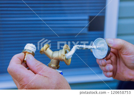 Worker holds brass fitting in one hand applies sealant with tool preparation for plumbing work. 120658753