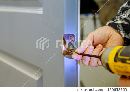 Worker on installing door latch using screwdriver, setting is tidy room, showcasing DIY skills during construction work Worker on installing door latch using screwdriver, setting is tidy room, showcasing DIY skills during construction work 120658763