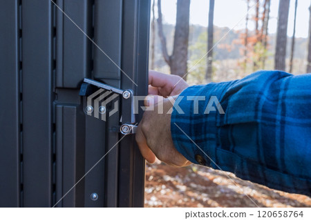 Worker installing closing securing metal gate at shed in forested location, backyard Worker installing closing securing metal gate at shed in forested location, backyard 120658764