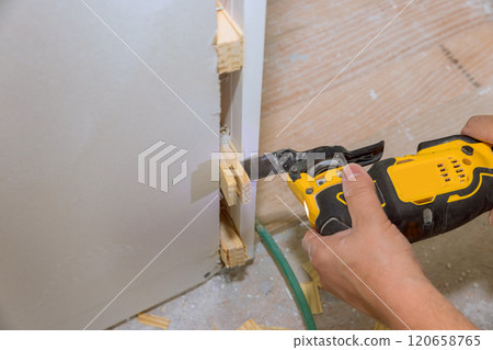 Worker uses handheld power tool to cut wooden pieces during home renovation during installation door construction unfinished flooring. Worker uses handheld power tool to cut wooden pieces during home renovation during installation door construction unfinished flooring. 120658765
