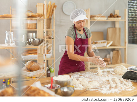 Girl works as baker in bakery, molds sausages from dough, rolls long round strips from dough Girl works as baker in bakery, molds sausages from dough, rolls long round strips from dough 120659209