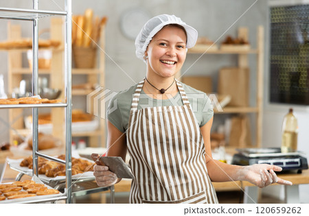 Portrait of cheerful baker girl with knife cutting raw dough in kitchen of private bakery Portrait of cheerful baker girl with knife cutting raw dough in kitchen of private bakery 120659262