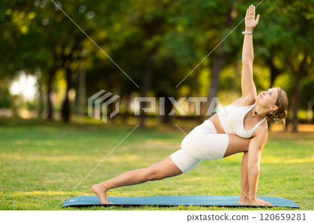 Girl performing Parivrtta Parsvakonasana twisting asana in summer park 120659281