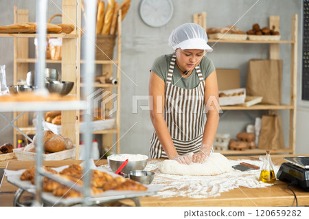 Woman works in bakery as baker, kneads dough, works with flour. 120659282