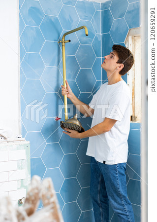 Focused guy assembling shower set before fixing to wall Focused guy assembling shower set before fixing to wall 120659291