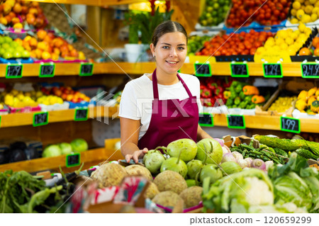 Young saleswoman working and posing in store near counter with round bottlegourd vegetable Young saleswoman working and posing in store near counter with round bottlegourd vegetable 120659299