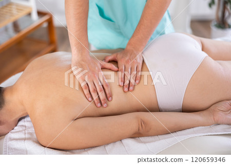 Masseur doing back massage to adult woman 120659346