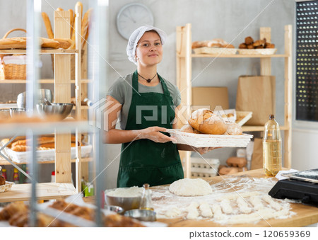 Young woman baker are standing near product range in bakery kitchen with basket of bread. Young woman baker are standing near product range in bakery kitchen with basket of bread. 120659369