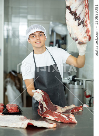 Positive young salesman demonstrating piece of meat in butcher shop Positive young salesman demonstrating piece of meat in butcher shop 120659381