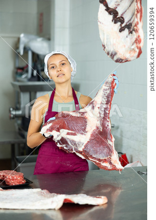 Positive young saleswoman demonstrating piece of meat in butcher shop 120659394