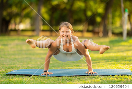 Girl in park on green grass of lawn performs Bhujapidasana 120659404