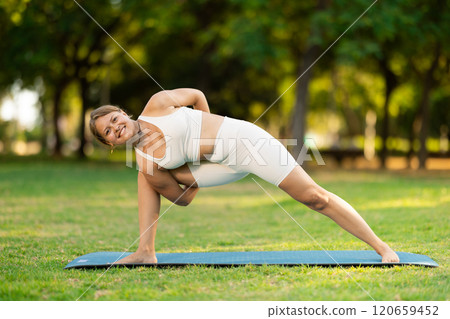 Young woman performing Baddha Parsvakonasana on green meadow 120659452