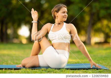 Girl in park on green grass of lawn performs lord of fishes, Matsyendrasana 120659460