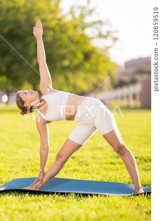 Smiling girl doing Triangle Pose Trikonasana on green meadow 120659519