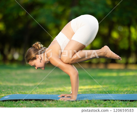 Smiling girl performing Bala Kakasana in green summer park Smiling girl performing Bala Kakasana in green summer park 120659583