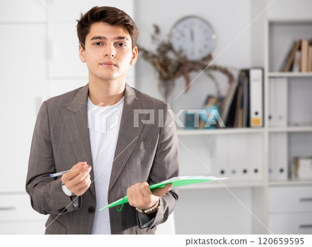 Positive man office worker holding folder in hands and looking at camera 120659595