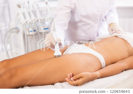 Aesthetician administering high frequency ultrasound procedure on woman thighs 120659643