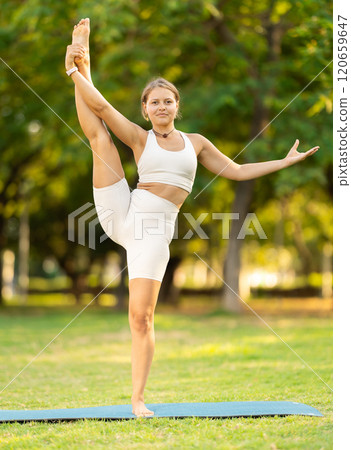 Girl in park on green grass of lawn performs Utthita Hasta Padangushthasana 120659647