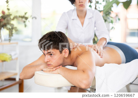 Masseuse doing back massage to young guy Masseuse doing back massage to young guy 120659667