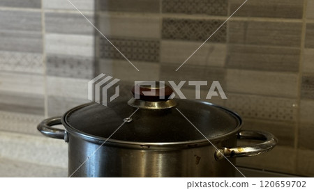 A modern cooking pot stands out on a tidy kitchen counter with stylish patterned tiles in the background 120659702