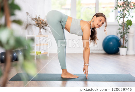 Young woman yoga trainer performing forward bend pose on black rug Young woman yoga trainer performing forward bend pose on black rug 120659746