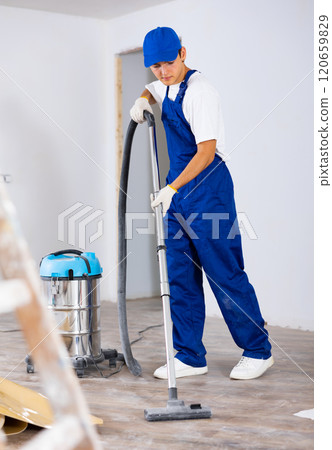 Young builder vacuuming floor while cleaning room in building after renovation Young builder vacuuming floor while cleaning room in building after renovation 120659829