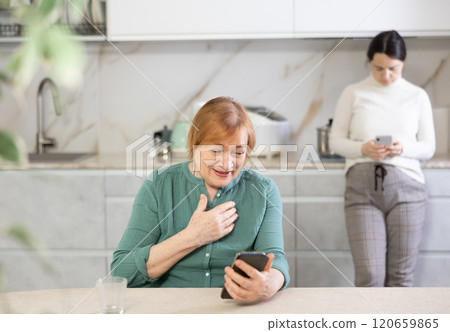 Positive mature woman and girl in kitchen with phone in hand communicates in social network 120659865