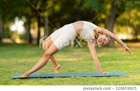 Girl performing Camatkarasana yoga asana in green sunlit park Girl performing Camatkarasana yoga asana in green sunlit park 120659925