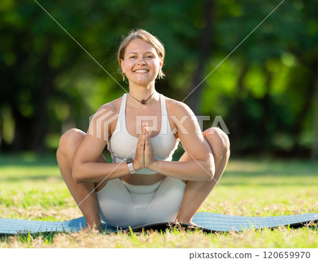 Girl in park on green grass of lawn performs Malasana 120659970