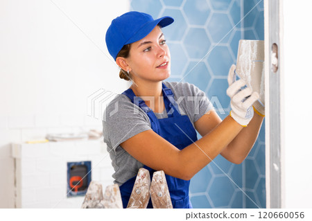 Young woman tiler glues ceramic tiles on the wall Young woman tiler glues ceramic tiles on the wall 120660056