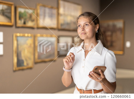 Woman with phone in hands view pictures and icons in museum hall Woman with phone in hands view pictures and icons in museum hall 120660061