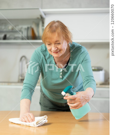 Happy mature woman cleaning her kitchen with radiant smile 120660070
