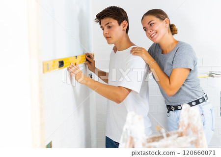 Young couple uses a spirit level on the wall Young couple uses a spirit level on the wall 120660071